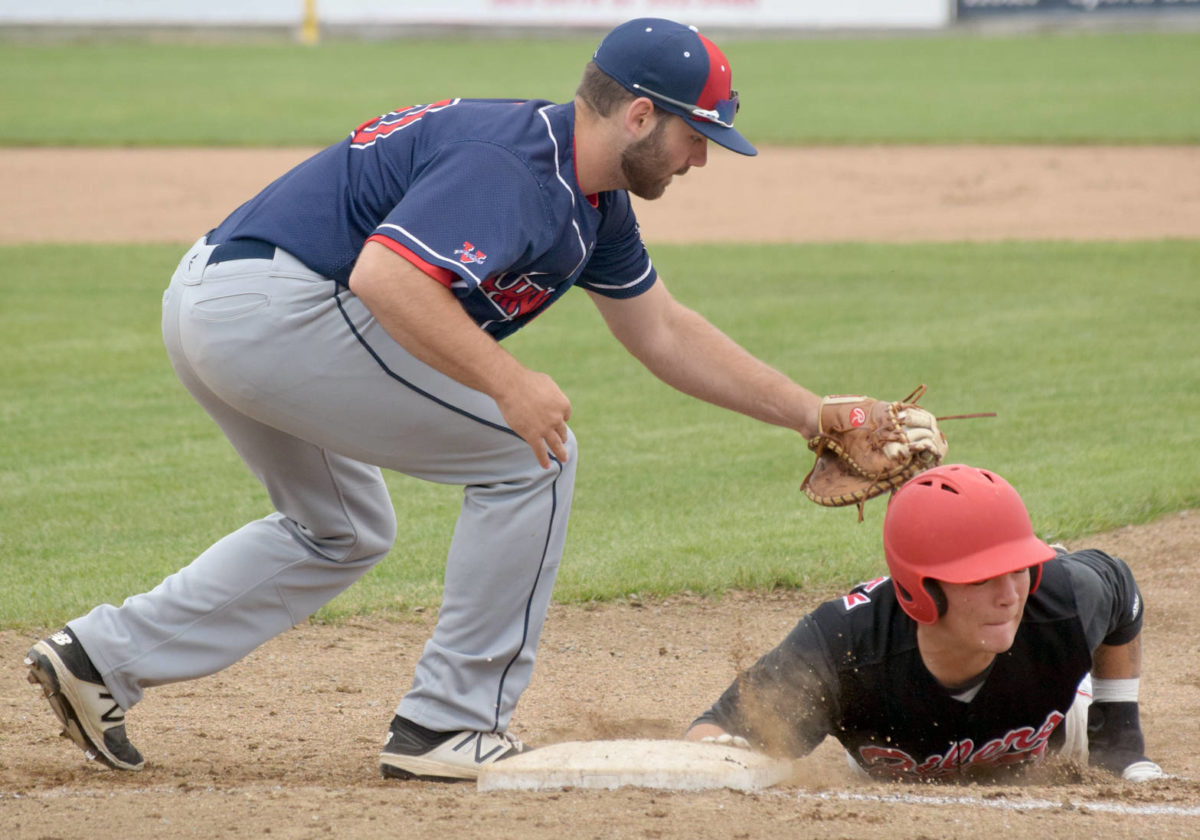 Peninsula Oilers shortstop Evan Berkey slides under the tag of Chugiak-Eagle River Chinooks first baseman Danny Dopp on Sunday, June 24, 2018, at Coral Seymour Memorial Park in Kenai. (Photo by Jeff Helminiak/Peninsula Clarion)