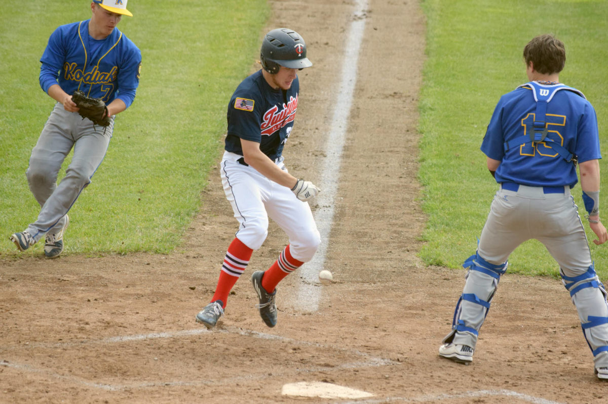 Jeremy Kupferschmid of the Twins scores in the fourth inning Monday, June 25, 2018, at Coral Seymour Memorial Park in Kenai after Kodiak pitcher Shaun Walton dropped the ball on the tag. Kodiak catcher Nathan James looks on. (Photo by Jeff Helminiak/Peninsula Clarion)