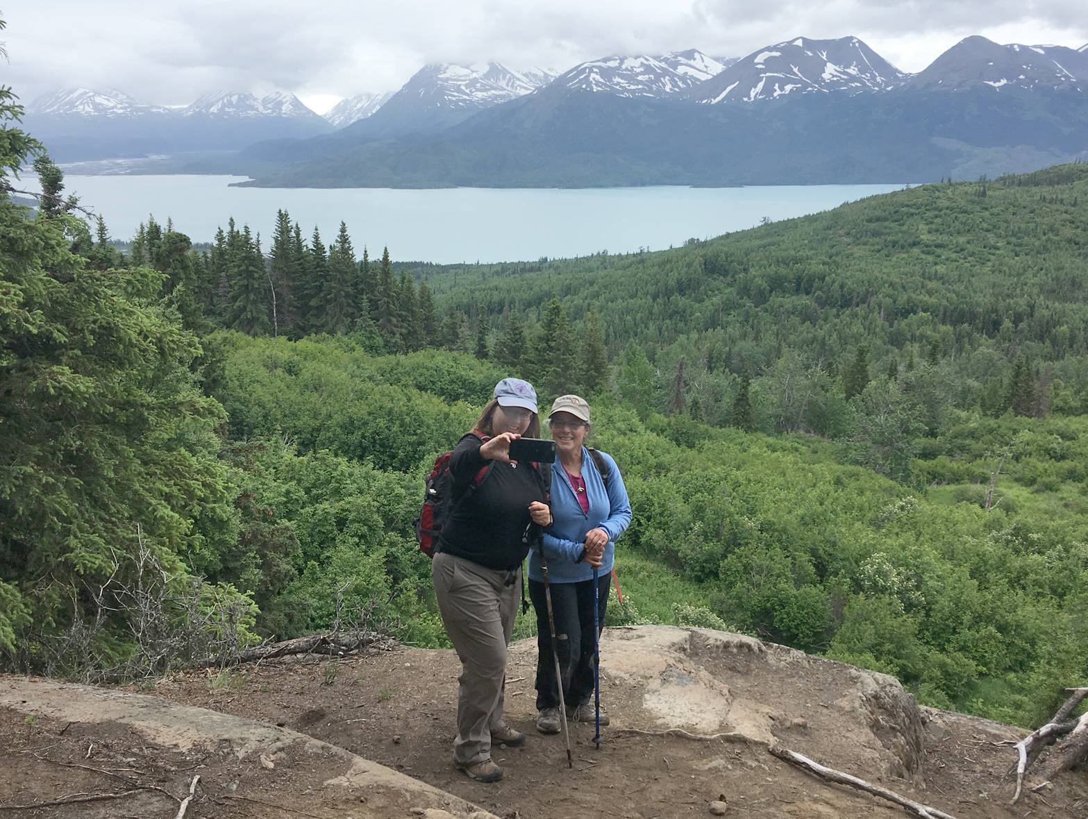 Sandy Kerns of Soldotna and Deborah Green of Moose Pass pause for a photograph during Take a Hike on the Bear Mountain trail Friday, June 29, 2018. Skilak Lake is in the background. (Photo by Jeff Helminiak/Peninsula Clarion)