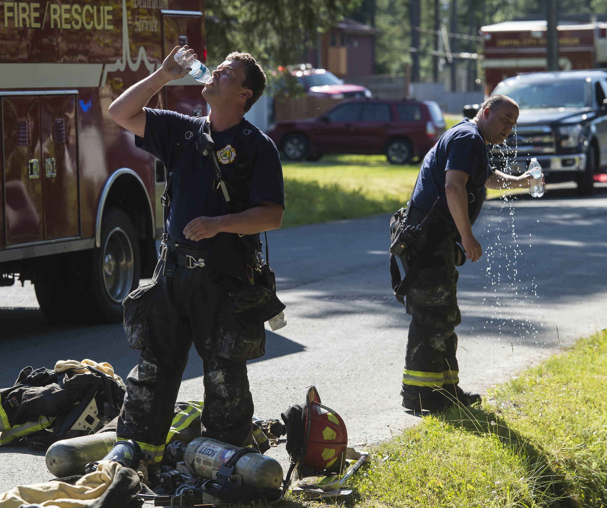 Capital City Fire/Rescue firemen attempt to cool off after fighting a house fire at 8460 Kimberly Street on Friday, July 20, 2018. (Michael Penn | Juneau Empire)