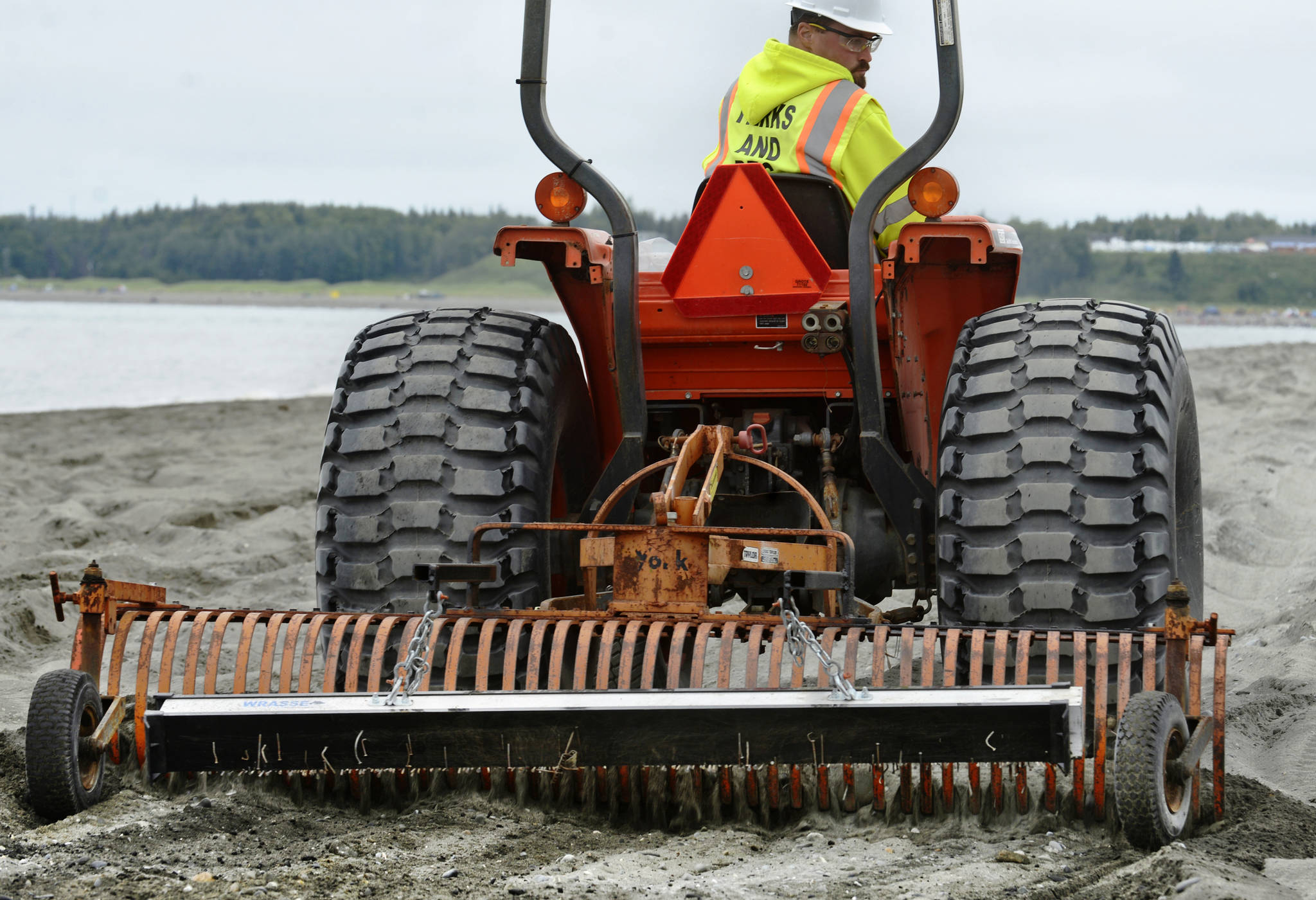 Kenai Parks and Recreation employee Jacob Hart rakes Kenai’s south beach to demonstrate how the magnetic bar hanging behind his rake picks up nails and other metal debris buried under the sand, on Friday, July 20, 2018 in Kenai, Alaska. The idea of using a magnetic rake to sweep up metal objects — left after many years of pallet bonfires, lost tent stakes, and general litter — came from Kenai Central High School sophmore Riley Graves, who created a magnetic leaf-rake prototype for this April’s Caring for the Kenai competition. Kenai Public Works Department shop foreman Randy Parrish built the rake after Graves’ idea, which he presented to the Kenai City Council on May 16. Since the July 10 beginning of this summer’s personal use dipnet fishery, Hart said the rake’s been deployed every evening. “When you drive over a dark spot in the sand, where you can tell it’s been a fire pit, you can hear the nails going tink, tink, tink,” he said. (Ben Boettger/Peninsula Clarion)