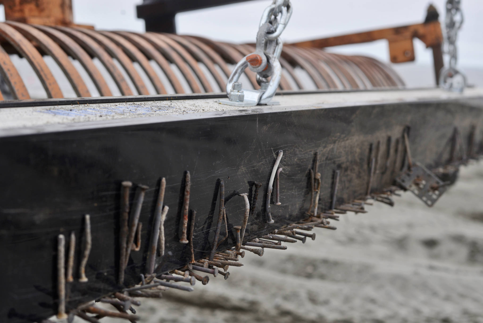 A variety of nails, screws, and staples pulled from the sand of Kenai’s south beach are stuck to a magnetic bar hanging behind a Kenai Parks and Recreation Department tractor rake on Friday, July 20, 2018 in Kenai, Alaska. Kenai shop foreman Randy Parrish, who built the adjustable chain suspension system, said the magnet can pick up a nail from eight inches away, making it able to pick up nails buried deep in the sand when hung low. (Ben Boettger/Peninsula Clarion)