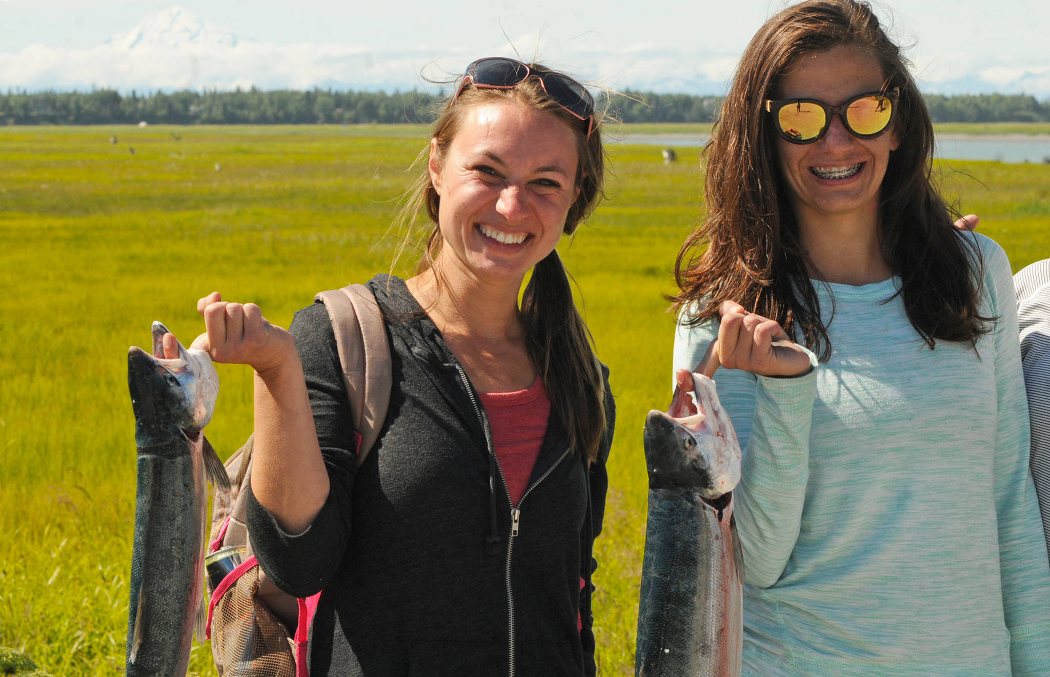 Anchorage residents Megen Draeger (left) and Athena Mallis (right) hold up the sockeye salmon they caught dipnetting in the Kenai River on Saturday, July 21, 2018 in Kenai, Alaska. (Photo by Elizabeth Earl/Peninsula Clarion)