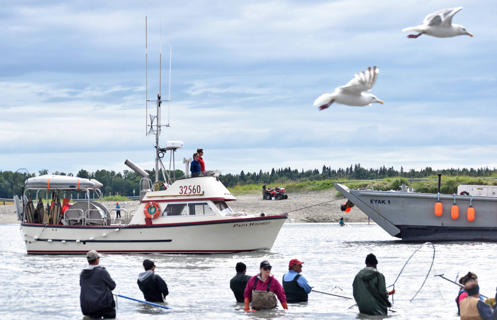 A commercial fishing vessel motors slowly past lines of personal-use dipnet fishermen in the mouth of the Kasilof River on Tuesday, July 31, 2018 in Kasilof, Alaska. (Photo by Elizabeth Earl/Peninsula Clarion)