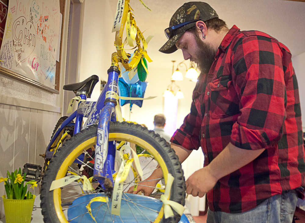 Photo by Rashah McChesney/Peninsula Clarion  Ben Griess hangs a ribbon upon which he wrote "Gone Home" on a bicycle Tuesday Feb. 18, 2014  in the lobby of the  Soldotna Nazarene Church where a memorial for Floyd Murphy was held in Soldotna, Alaska. Murphy Thursday after a swimming accident.