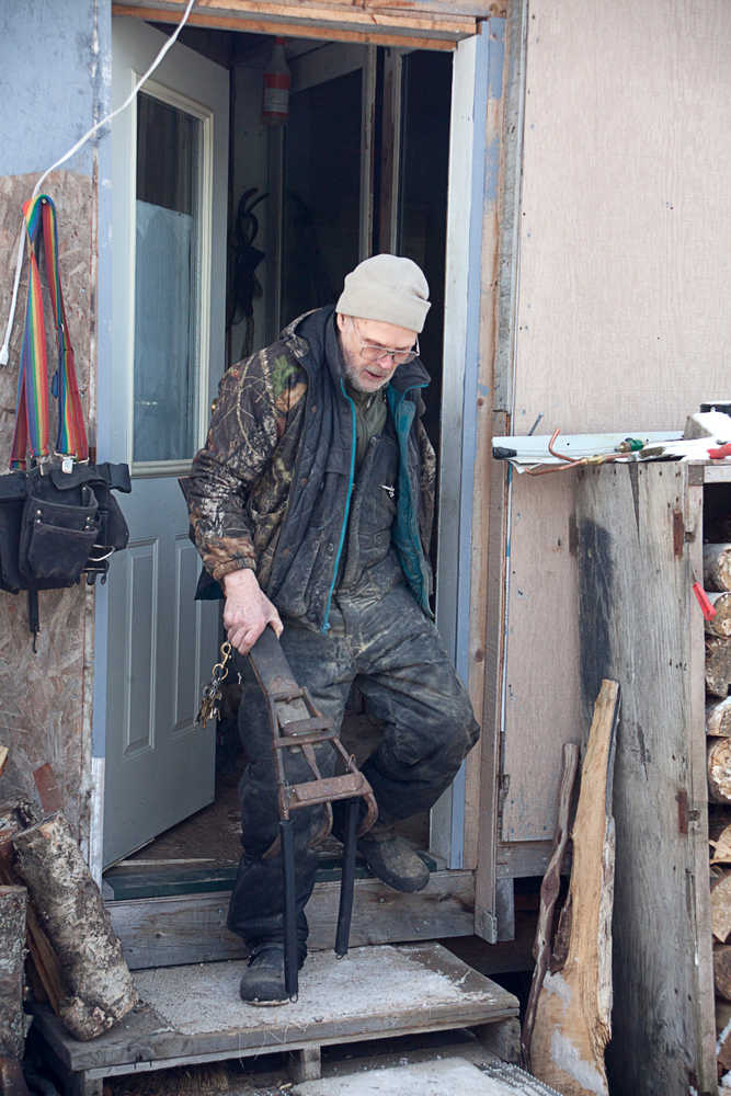 Photo by Rashah McChesney/Peninsula Clarion  Cliff Sisson, of Kasilof, walks out of his house with a braking mechanism for a wooden Iditarod sled he and two companions are building Thursday Feb. 20, 2014 in Kasilof, Alaska.
