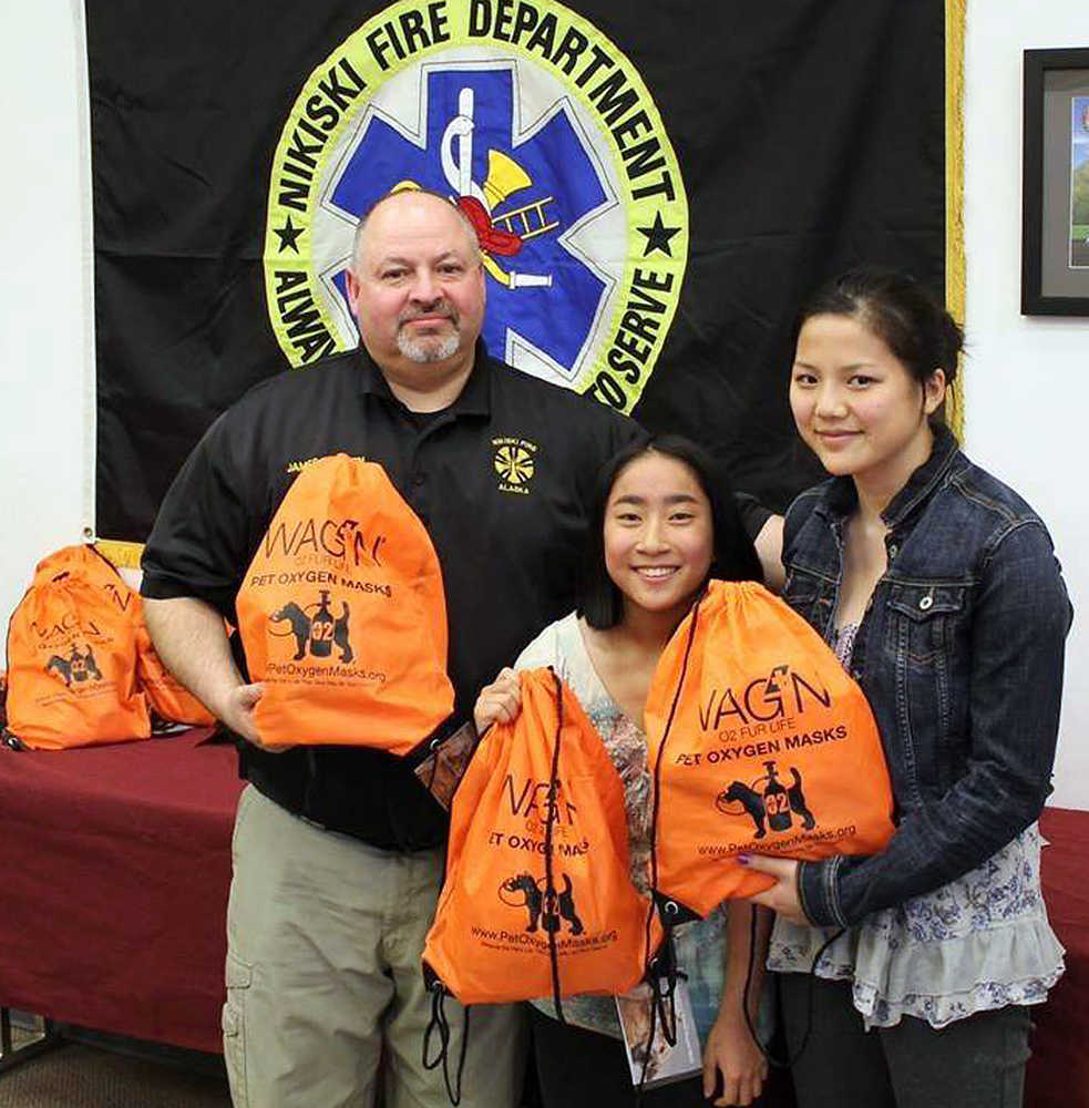 Photo courtesy Denise Cox Marguerite and Evangeline Cox pose with Nikiski Fire Chief James Baisden at the Nikiski Fire Board meeting on April 16. The two girls, sophomores at Nikiski High School, donated 12 pet oxygen masks to the Nikiski department and seven to the Kenai Fire Department.