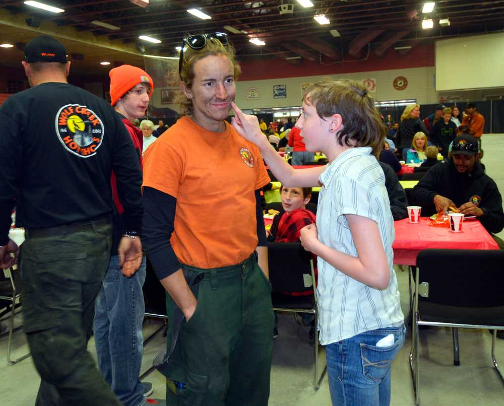 Photo by Dan Balmer/Peninsula Clarion Mickinzie Ticknor from Soldotna wipes the soot off of firefighter Erin Kimsey's face at the firefighter appreciation dinner Sunday at the Soldotna Regional Sports Complex. Ticknor said she wants to be a firefigher when she gets older. Kimsey, a member of the Wolf Creek Hotshots from Glide, Oregon, said the support from the community has been amazing.