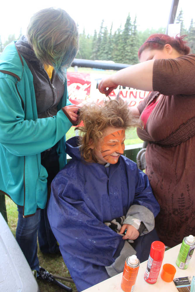 Photo by Kelly Sullivan/ Peninsula Clarion Oria Stocks sits patiently as Sarah Overpeck and Celeste Kent tease her hair into a giant mane to match her tiger face paint,Frontier Community Services World Series Baseball, Saturday, June 21.