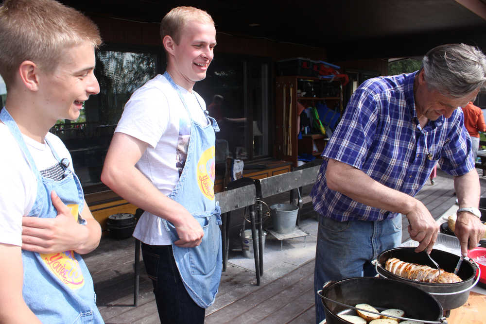 Photo by Kelly Sullivan/ Peninsula Clarion Jonas Vikstrom and Sebastian Gabriel watch Nels Anderson cut up a pork dish inside a Dutch oven, Saturday, July 19, in Soldotna.