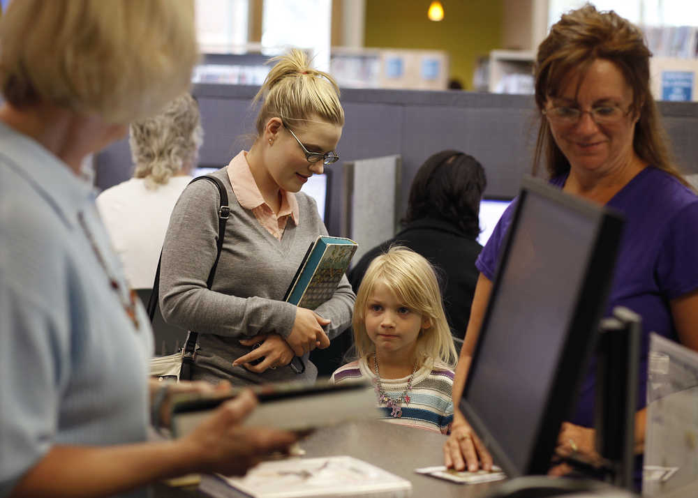 Photo by Rashah McChesney/Peninsula Clarion  Ally Schuetzler glances at her daughter Riley Schuetzler, 5, as the two check out a book at the Kenai Community Library Tuesday July 23, 2014 in Kenai, Alaska.