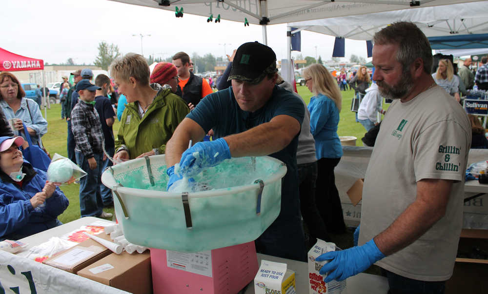 Glen Faulkner, right, and James Slone, center, work the cotton candy machine at the Hilcorp tent while Laura Favretto, left, hands out their wares during Industry Appreciation Day Saturday on the green strip in Kenai.