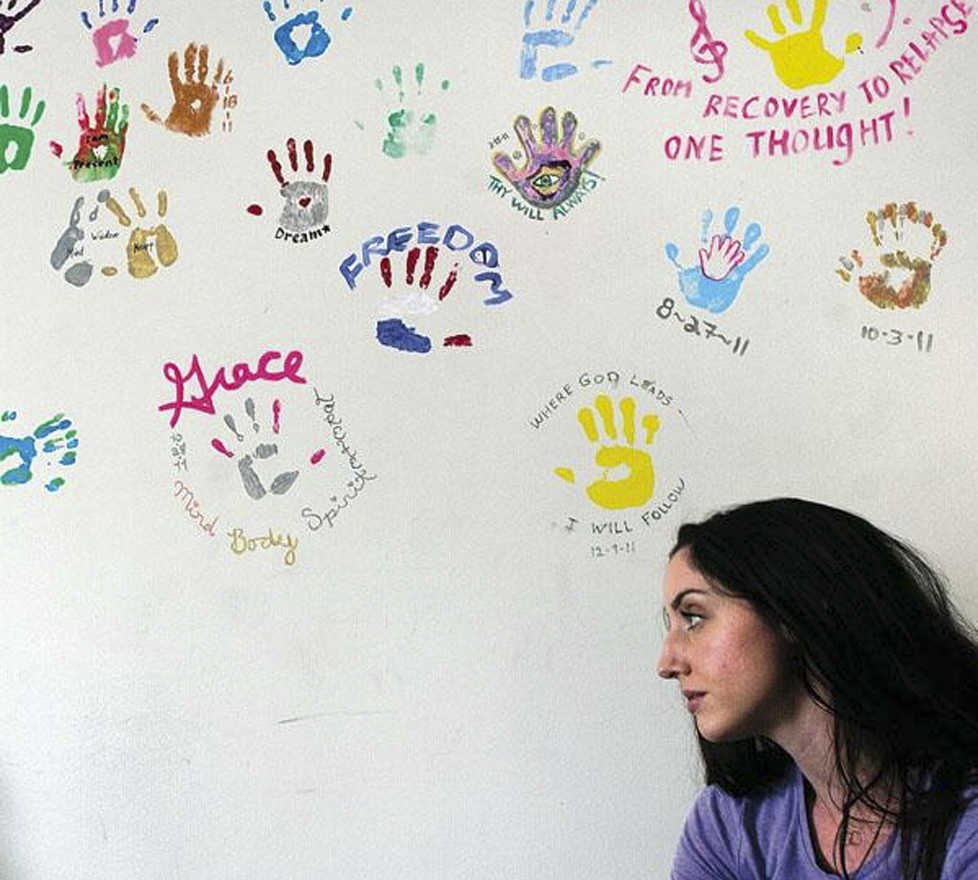 Clarion file photo Kelsey Cusack, volunteer Yoga teacher at the Serenity House treatment center, stands near a wall of handprints made by previous graduates of the substance abuse program. The organization is screening a documentary about addiction on Sunday at the Orca Theater in Soldotna.