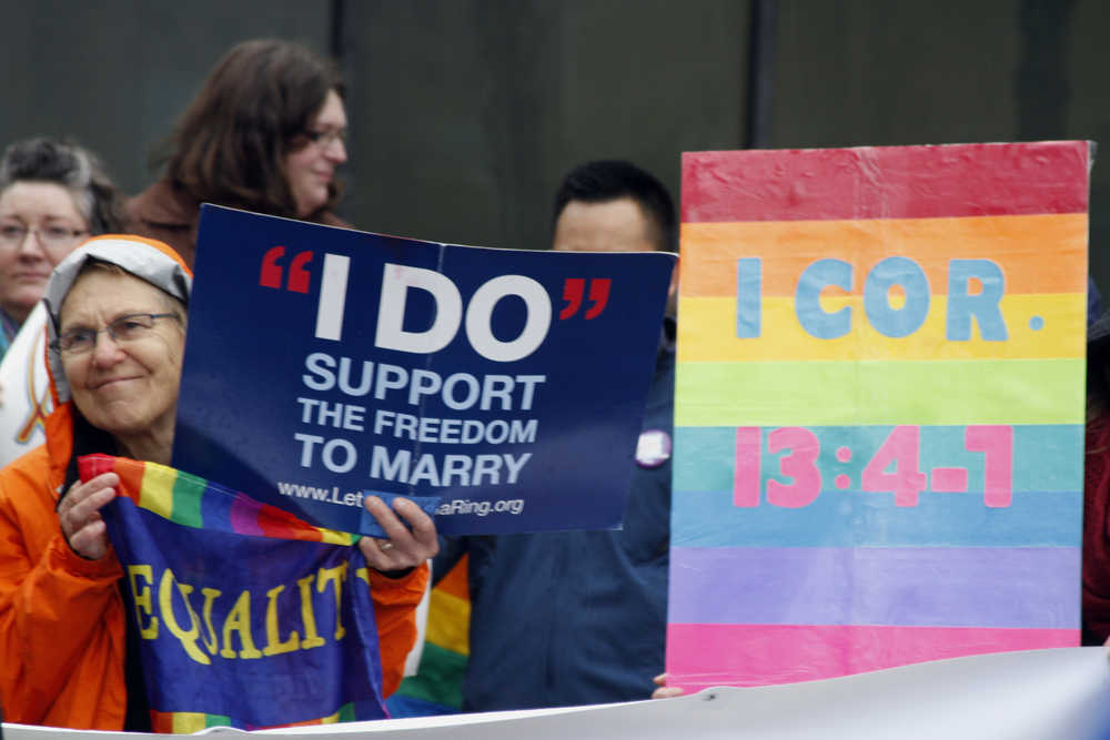 Lin Davis, of Juneau, Alaska, shown wearing an orange rain coat, holds signs supporting gay marriage during a news conference Friday, Oct. 10, 2014, outside the federal courthouse in Anchorage, Alaska. A federal judge on Friday heard arguments from five gay couples seeking to overturn the state's ban on gay marriage. (AP Photo/Mark Thiessen)