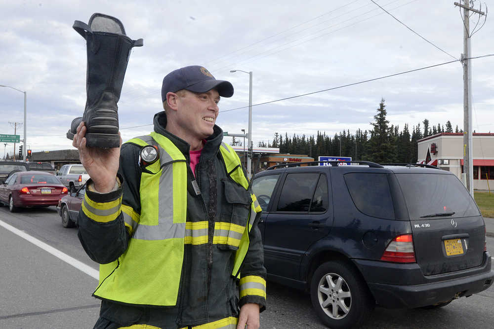 Photo by Rashah McChesney/Peninsula Clarion  Kenai firefighter Justin Horton waves a boot in the air for drivers along the Kenai Spur Highway Friday October 17, 2014 in Kenai, Alaska.  Several off-duty firefighters stood near the intersection of Bridge Access Road and the highway soliciting donations for the Muscular Dystrophy Association.