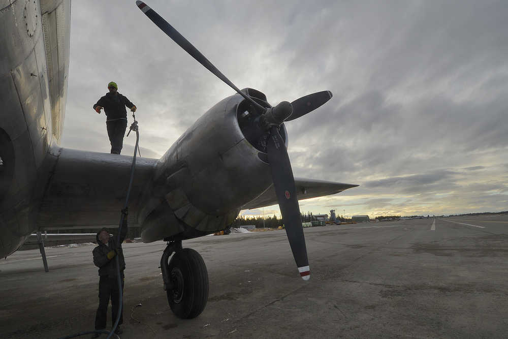 Photo by Rashah McChesney/Peninsula Clarion Spencer Wyman gives a fuel line to Zachary Sawyer as the two refill a WWII-era plane used by Everts Fuel Service on Tuesday Jan. 13, 2014 at the Kenai municipal airport in Kenai, Alaska.
