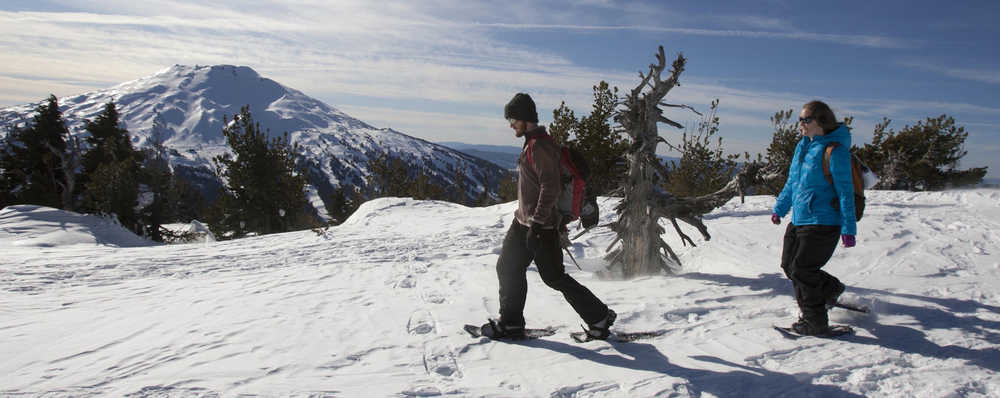 File--In this Feb. 6, 2012 photo, with Mount Bachelor in the distance, from left, Denny Knowles, 29, and his wife Natasha Knowles, 28, enjoy the view from the top of Tumalo Mountain, Ore., during a snowshoe trip.  Snowshoeing does not require as much gear and as many logistics as other wintertime sports such as cross-country skiing or downhill skiing and snowboarding. You basically just strap on the shoes and go. (AP Photo/The Bulletin, Andy Tullis, file)