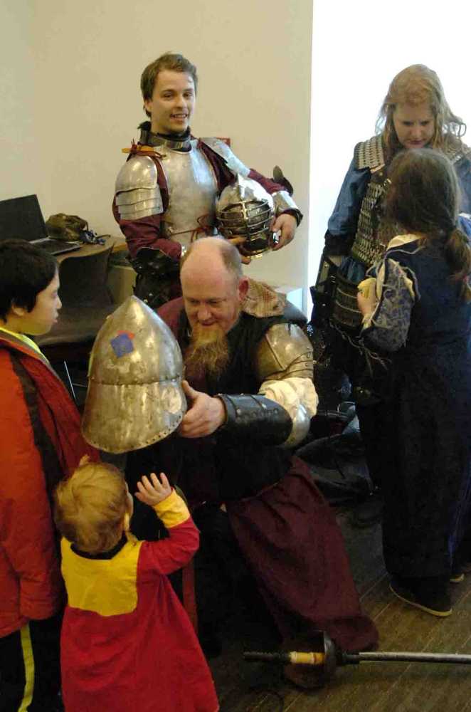 Ben Boettger/Peninsula Clarion David Ekholm, known as Nikor from the Isle of Oaks, lets a visitor try on his helm during the Society for Creative Anachronisms Newcomers Feast at the Soldotna Public Library on Saturday, March 14.
