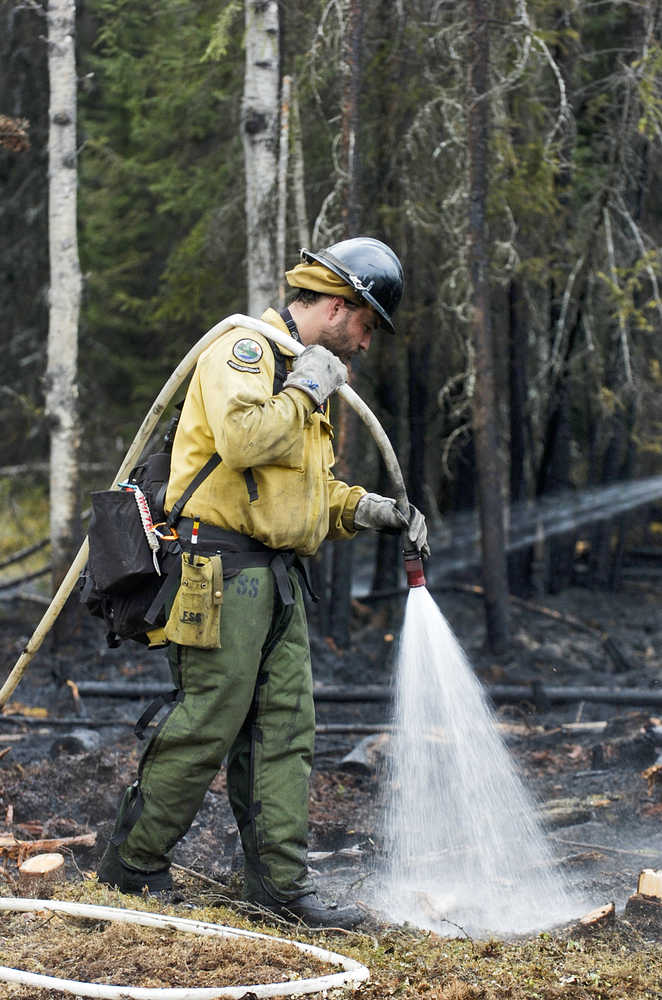 Photo by Rashah McChesney/Peninsula Clarion  Nick Adamson, a wildland fire and resource technication with the state's Division of Forestry, wets the ground at the Robin Avenue wildfire where a one-half acre piece of land was charred Sunday May 24, 2015 in Funny River, Alaska. The fire was started with a man's burn pile got away from him.