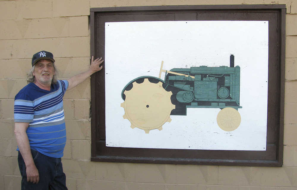 ADVANCE FOR RELEASE MONDAY MAY 25, 2015 AND THEREAFTER In this May 13, 2015 photo, artist Dan Bates poses with a mural he painted 25 years ago at the North Pole Grange in North Pole, Alaska. About 25 years ago, a judge ordered artist Dan Bates to paint a mural as the penalty for a youthful indiscretion. The painting of a tractor is still featured on the side of the North Pole Grange, which was built in 1964 to promote agriculture in the Interior. (Amanda Bohman/Fairbanks Daily News-Miner via AP)