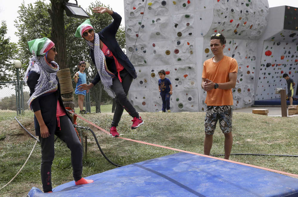 In this picture taken on Friday, May 29, 2015, female Iranian slackliner Samaneh Hasanzadeh balances on a slackline while she is watched by her sister, left, and instructor Hamed Heidari in a sports club in Tehran, Iran.  (AP Photo/Vahid Salemi)