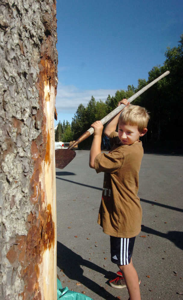 Photo by Megan Pacer/Peninsula Clarion Joshua Berson, 8, scrapes bark off his father's log in preparation for the Sawfest Chainsaw Carving Competition on Thursday evening at Stanley Chrysler in Soldotna, Alaska. Berson's father, Eric Berson of The Dreamer's Woods in Sterling, is one of several participant's in this year's Sawfest, which will last from Thursday through Sunday as part of the Progress Days festival.