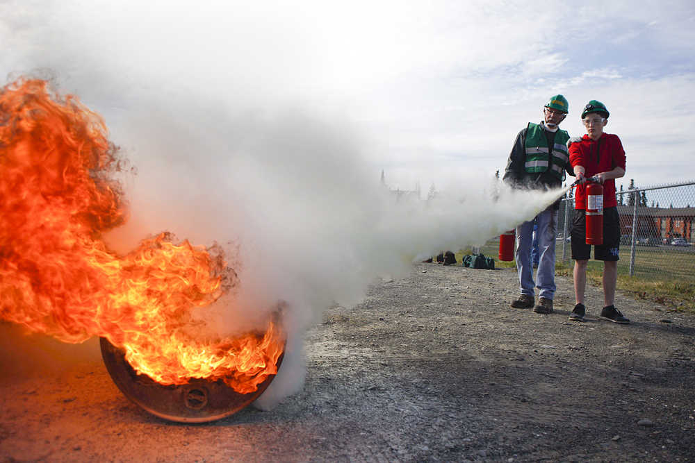 Photo by Rashah McChesney/Peninsula Clarion  John Eller, of Soldotna, helps William Gross, 14, extinguish a fire after a Community Emergency Response Team training drill on Saturday August 8, 2015 at the Soldotna Prep school in Soldotna, Alaska.