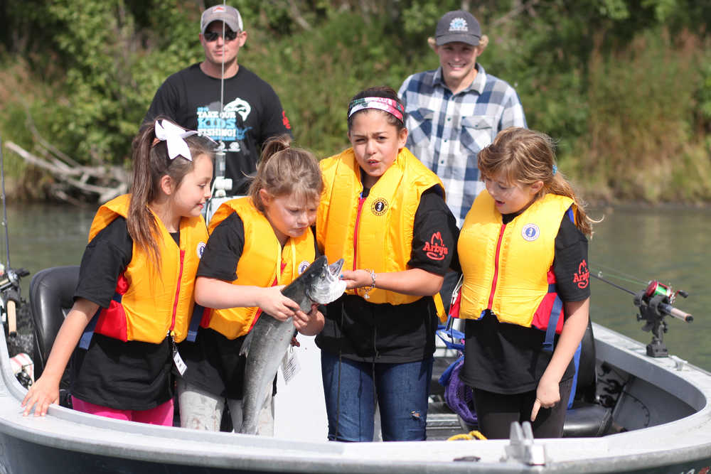 Ben Boettger/Peninsula Clarion  As their boat returns to the bank of the Kenai River, Aaliyah Bookey, Zoey Redfern, Alyssa Almeida, and Jessica Rumaner (pictured from left to right) examine a silver salmon caught by Rumaner during the Take Our Kids Fishing event at Soldotna's Centenial Park on Thursday, August 13.
