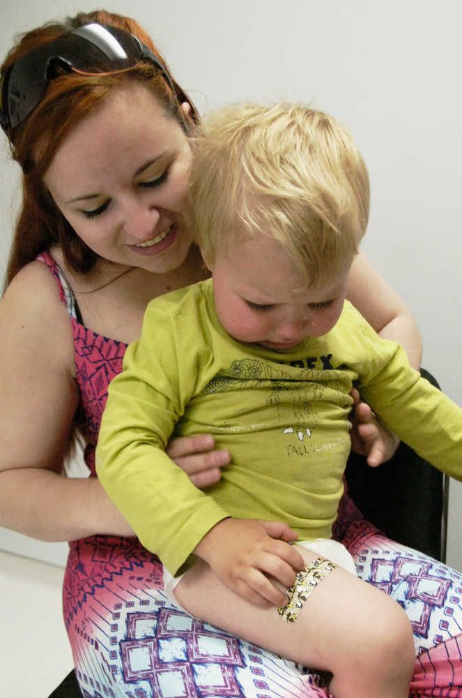 Ben Boettger/Peninsula Clarion Sitting on the lap of Megan Brown, a recently-vacinated Aushtin Orlob examines the band-aid on his thigh, where he recieved the shot, during the Kenai Health Center's Saturday Vacination Clinic on June 13.