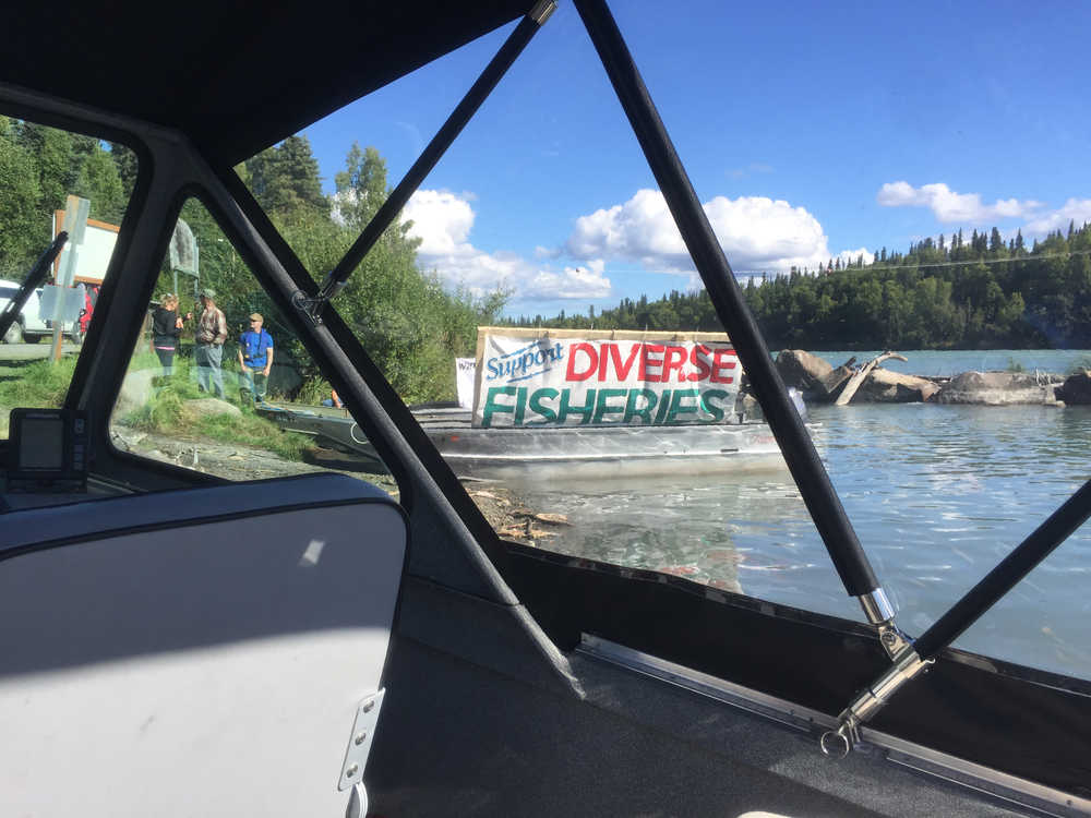 Photo by Rashah McChesney/Peninsula Clarion Dwight Kramer, member of the Kenai Area Fisherman's Coalition, watches revelers at a party during the Kenai River Sportfishing Association's annual Kenai River Classic as he floats down the Kenai River with a banner protesting the event and its founder, Bob Penney, on Wednesday August 19, 2015 in Soldotna, Alaska.