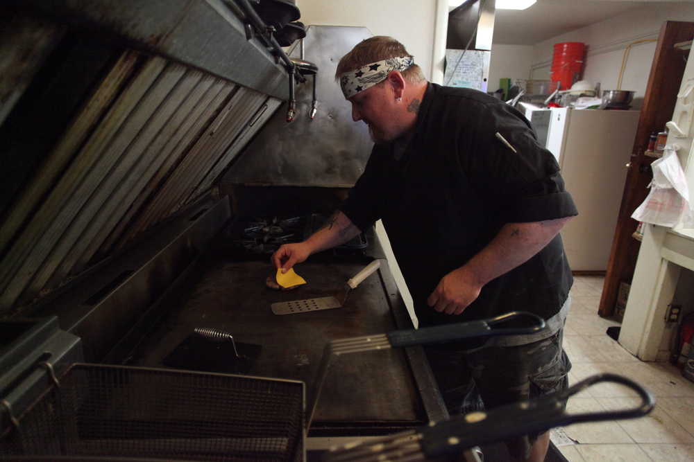 Photo by Kelly Sullivan/ Peninsula Clarion Richard Garrett prepares a burger for a customer Sunday, Aug. 23, 2015, at Garrett's Grill located inside The Place bar in Kenai, Alaska.