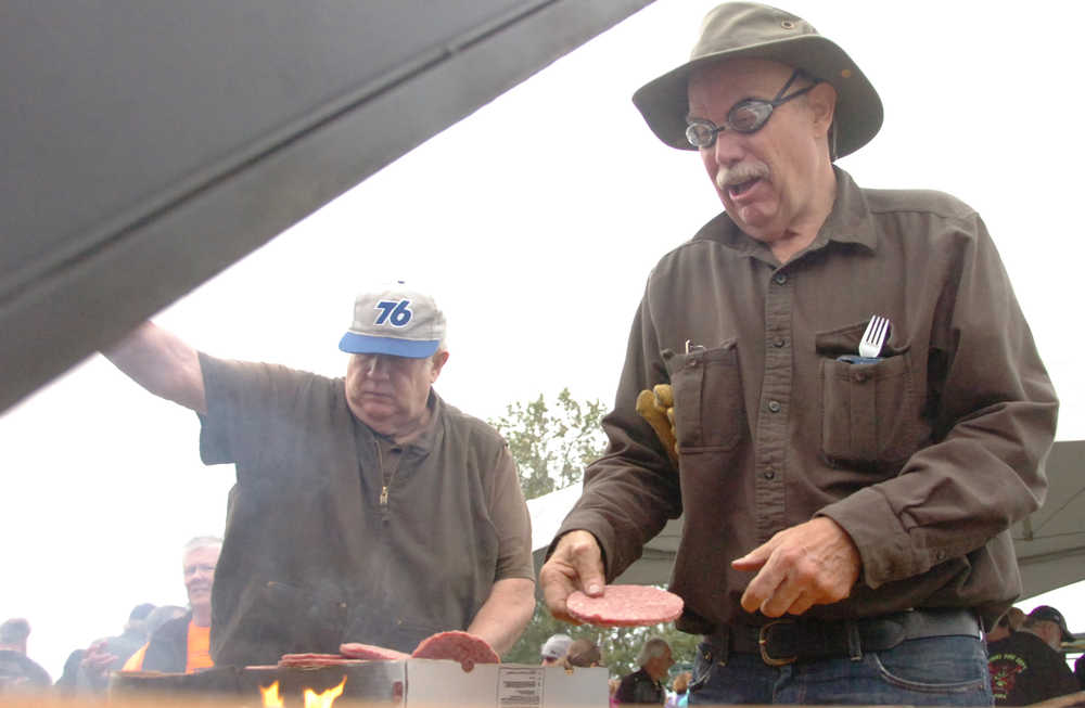 Ben Boettger/Peninsula Clarion Wearing swim goggles to protect his eyes from smoke, Bill Switzer tosses burger patties on a grill with the help of Larry Nudson (background) during Kenai's Industry Appreciation Days on Saturday, August 29 at the Kenai Park Strip.