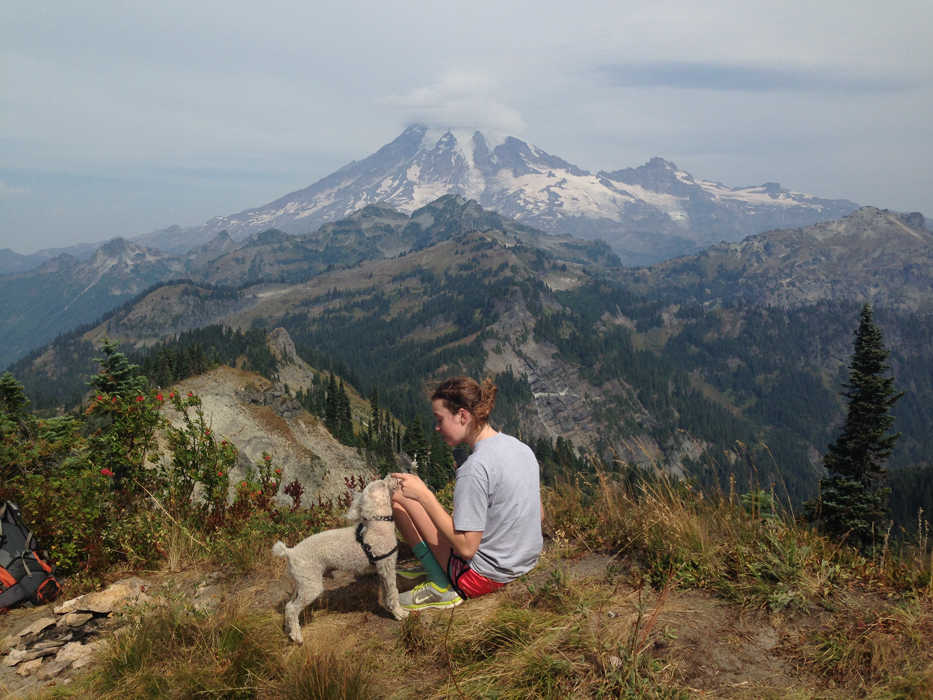 ADVANCE FOR WEEKEND EDITIONS, SEPT. 12-13 - In this photo taken Aug. 11, 2015, Kenzie Hill feeds Largent a bacon strip atop Tatoosh Peak, Wash., with Mount Rainier looming on the horizon.   October is national adopt-a-dog month, according to the American Human Society, the perfect time to pick up a new hiking partner. But before you hit the trail it's vital that you prepare your pup. (Craig Hill/(/The News Tribune via AP)  )