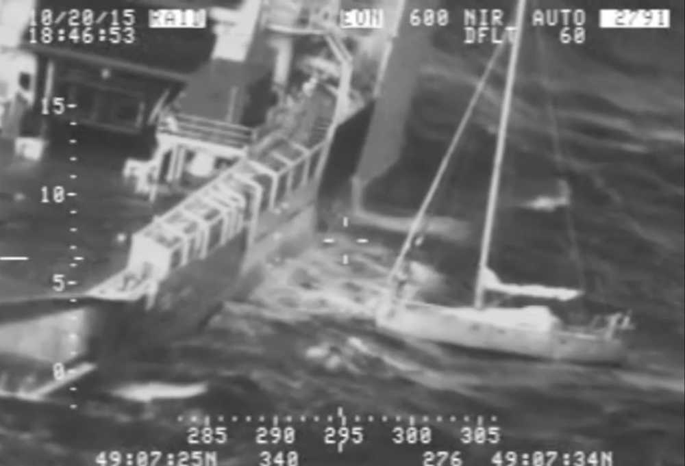 In this frame from video provided by the U.S. Coast Guard, a Frenchman with his cat tucked inside his clothing, at right, stands on his saildboat before making a leap Tuesday, Oct. 20, 2015, jumping to a waiting rescue ship, left, south of Alaska. The video shows the Frenchman on the rigging pole near the bow of his sailboat, riding wave after wave until making a dramatic leap over the railing of the Tor Viking. (Coast Guard via AP)