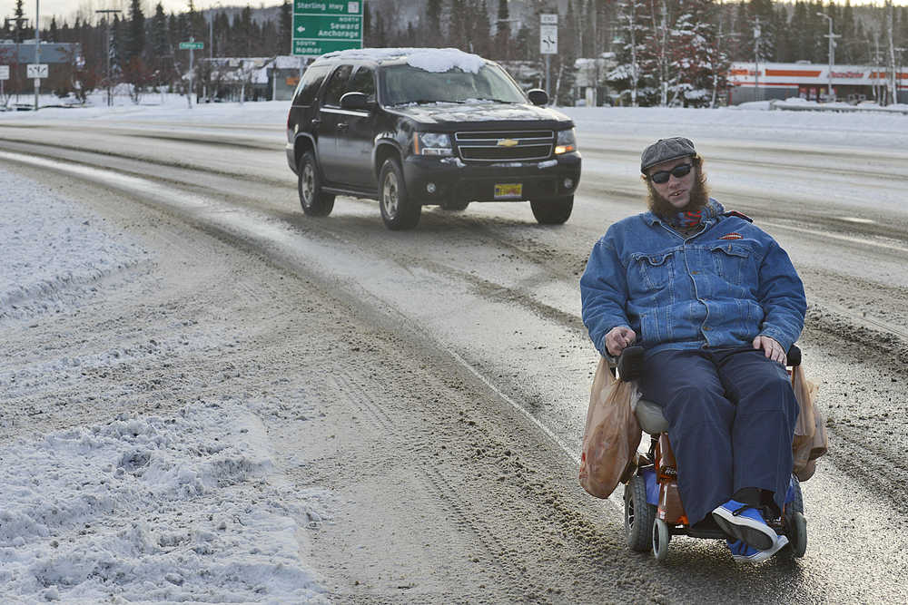 Photo by Rashah McChesney/Peninsula Clarion Jay Galloway motors his wheelchair down the Kenai Spur Highway after a heavy snow on Monday Nov. 9, 2015 in Soldotna, Alaska. Galloway could not ride on the sidewalks as they were still covered in snow.  "I understand that it takes time, but (the city) really needs to clear the sidewalks for the people who need them," he said.