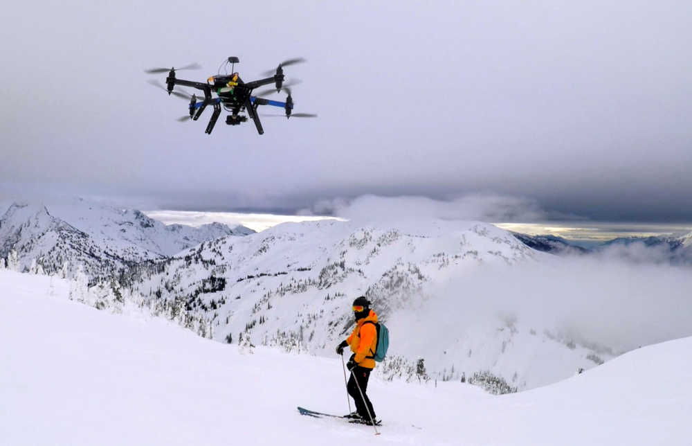 This Dec. 2014 photo shows a drone hovering by a skier as he makes his way down mountainside at resort at Revelstoke, B.C., Canada. Some US ski resorts are exploring the possibility of "drone zones" where professionally operated drones can produce customized video that show off individuals skiers in action. (Jason Soll/Cape Productions via AP)