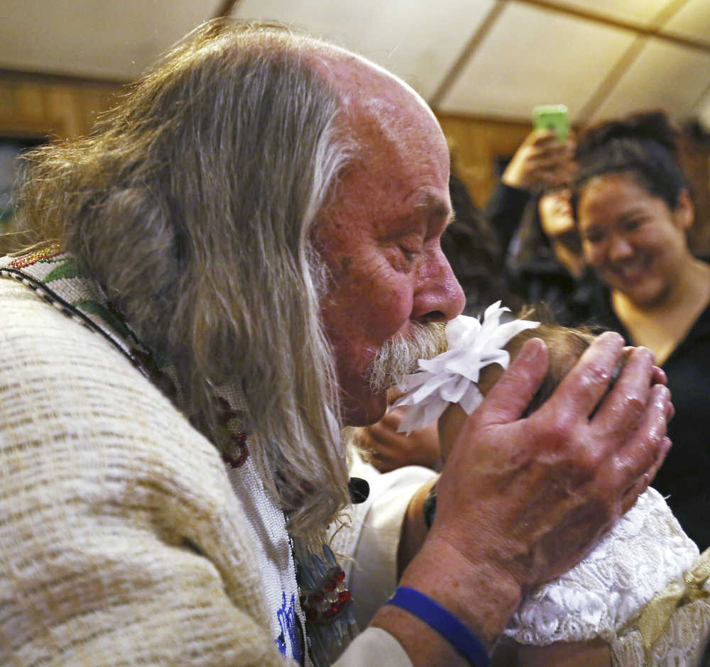 In this Nov. 18, 2015 photo, the Rev. Scott Fisher kisses 2-month old Elizabeth Miller during her Baptism at St. Matthew's Episcopal Church in Fairbanks, Alaska. With long hair, unruly sideburns and colorful Converse sneakers, Fisher is known to many as the "hippy" priest. (Eric Engman/Fairbanks Daily News-Miner via AP)