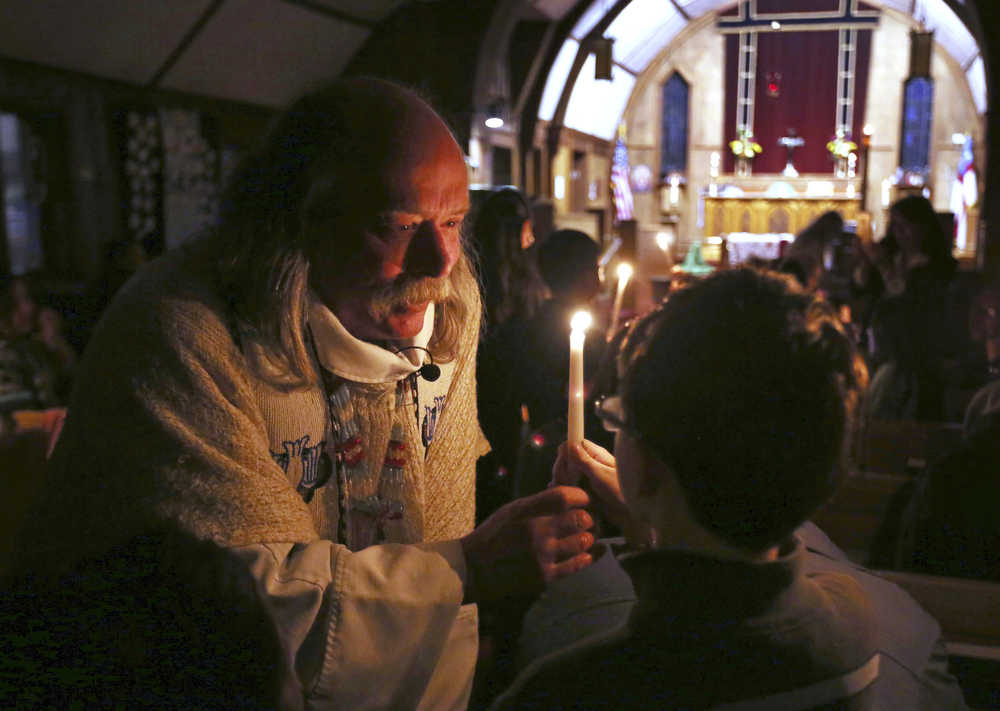 In this Nov. 18, 2015 photo, the Rev. Scott Fisher hands a Baptism candle to Aiden Taylor during a service at St. Matthew's Episcopal Church in Fairbanks, Alaska. With long hair, unruly sideburns and colorful Converse sneakers, Fisher is known to many as the "hippy" priest. (Eric Engman/Fairbanks Daily News-Miner via AP)