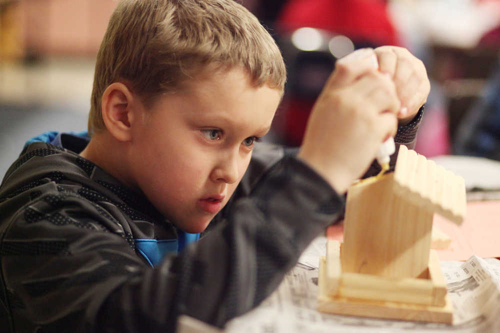 Photo by Kelly Sullivan/ Peninsula Clarion Second grader Noah Kalugin glues the roof onto his birdhouse during the Bites for Birds event, where Title I students were invited to learn how to make birdhouses with their parents after school Thursday, Dec. 3, 2015, at Mountain View Elementary School in Kenai, Alaska.