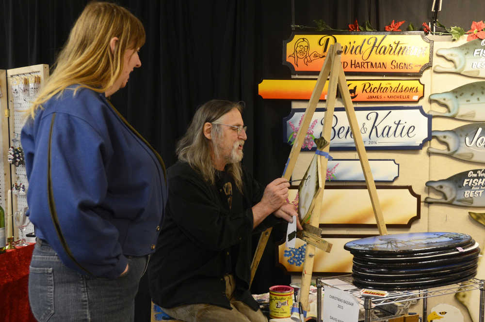 Photo by Megan Pacer/Peninsula Clarion Kenai resident Joyce Colbenson looks on as David Hartman, a painter, works on one of his handmade signs during the Annual Auxiliary Holiday Bazaar on Monday, Dec. 7, 2015 at Central Peninsula Hospital in Soldotna, Alaska. Money raised at the bazaar went to the Hospital Auxiliary Scholarship fund.