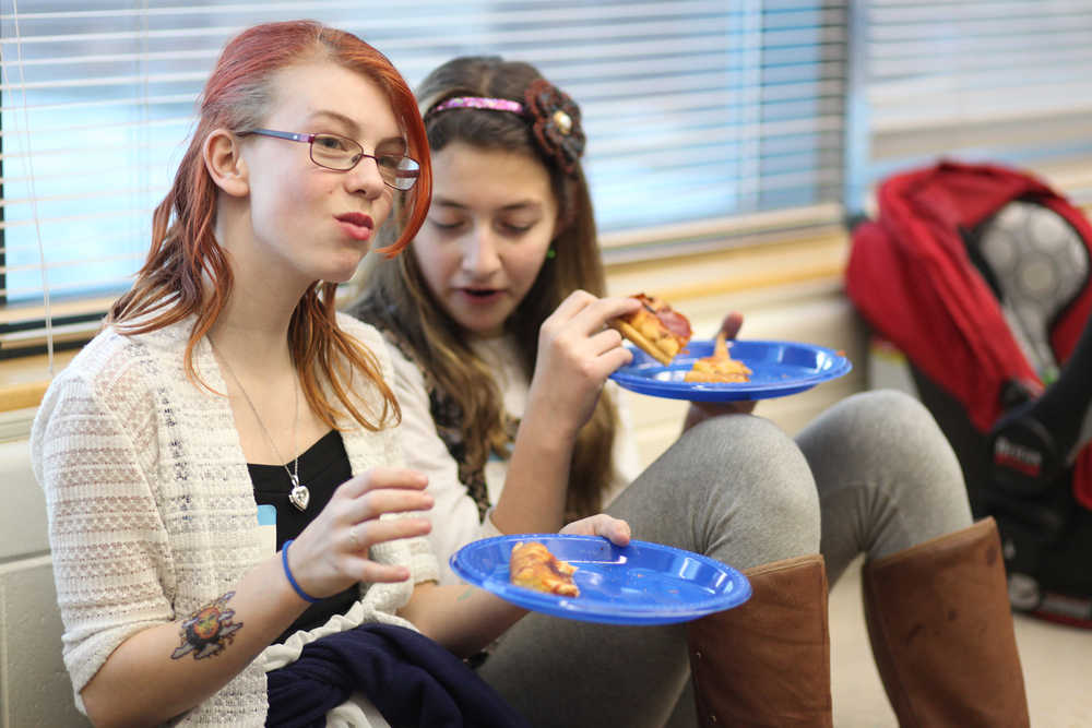 Photo by Kelly Sullivan/ Peninsula Clarion Two members of the Granny Wannabees, Nikiski-Middle High School's middle school knitting club, munch on pizza after the group officially presented their handmade blankets to staff from the Nikiski Senior Center Thursday, Dec. 10, 2015, in the school's library in Nikiski, Alaska.