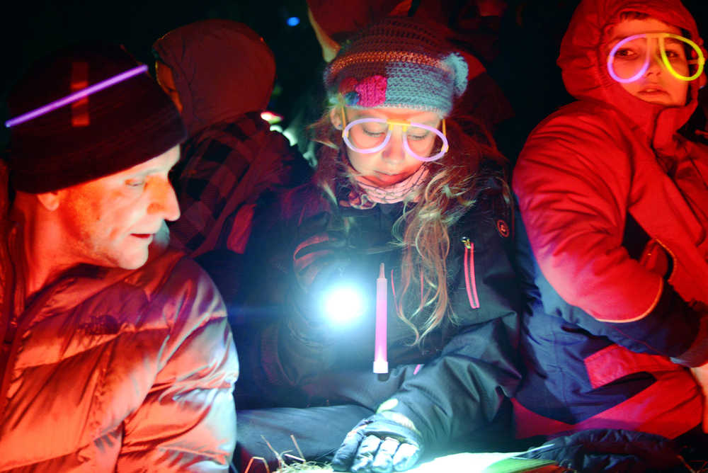 Ben Boettger/Peninsula Clairon Riding a haywagon through a residential Kenai neighborhood, Mountain View Elementary Principal Karl Kircher (left) leans over to read a Christmas carol while singing with students, their families and other members of the community. Mountain View students and staff went caroling through a neighborhood near the school before warming up at a bonfire with hotdogs and hot chocolate Friday.