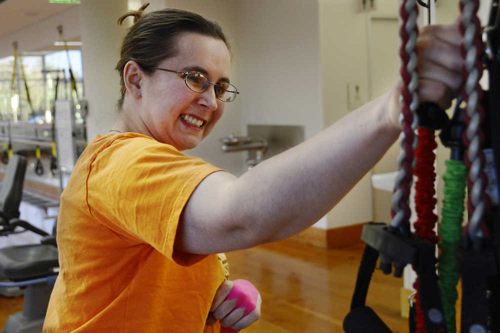 Ben Boettger/Peninsula Clarion Nicole Harmon reaches for a resistance band she will use in a rowing exercise, part of her physical therapy, on Thursday Dec. 10 at the Dena'ina Wellness Center in Kenai. Harmon's physical therapist Sabrina Royster said the exercise is "meant to help her brain re-educate the muscles of her arm to balance muscle contractions. "