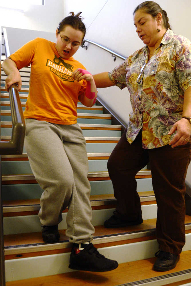 Ben Boettger/Peninsula Clarion Nicole Harmon (left) descends a staircase with the help of physical therapist assistant Sabrina Royster on Thursday, Dec. 10 at the Denai'ina Wellness Center in Kenai.