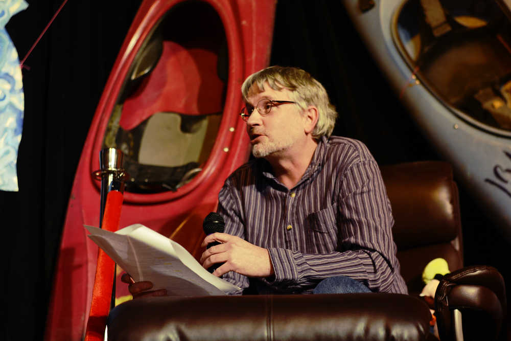 Ben Boettger/Peninsula Clarion Sitting on stage in an easy chair backed by decorative kayaks, outgoing director of the Kenai Watershed Forum Robert Ruffner plays himself in a skit satirically re-enacting his failed appointment to the state Board of Fisheries during an event held in his honor on Saturday, Jan. 9 at the Triumverate Theatre in Kenai.