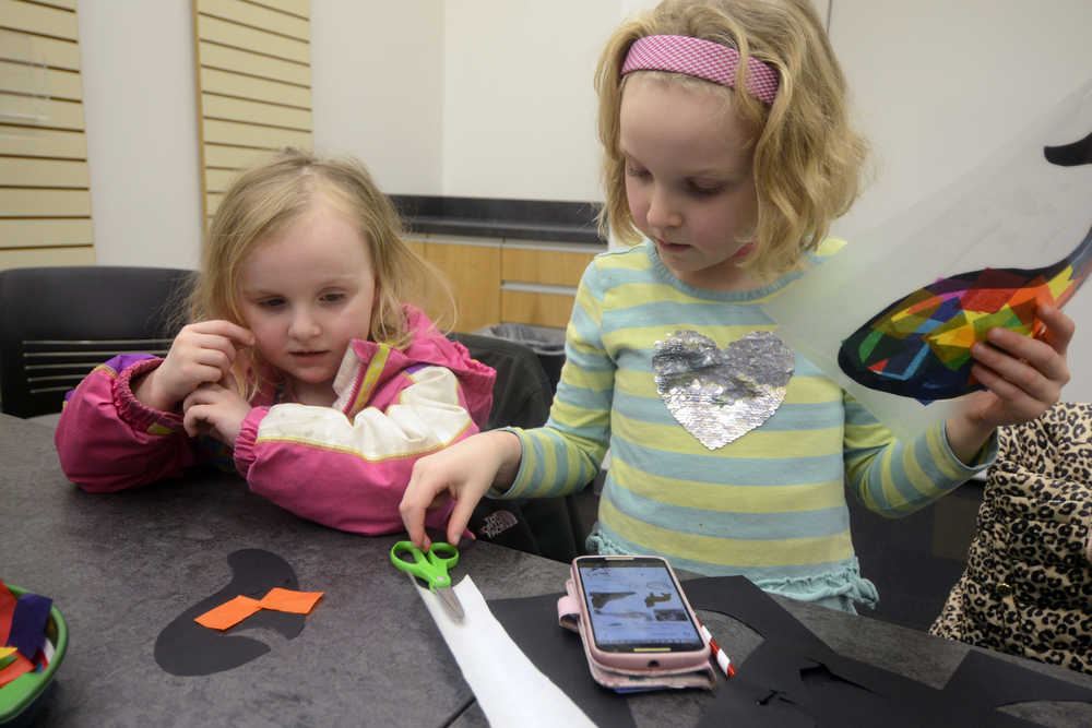 Photo by Megan Pacer/Peninsula Clarion Elsa Meyer, 6, helps her younger sister, 3-year-old Naomi Meyer, cut out a paper whale made to look like stained glass during a family craft night on Tuesday, Jan. 12, 2016 at the Kenai Community Library in Kenai, Alaska.