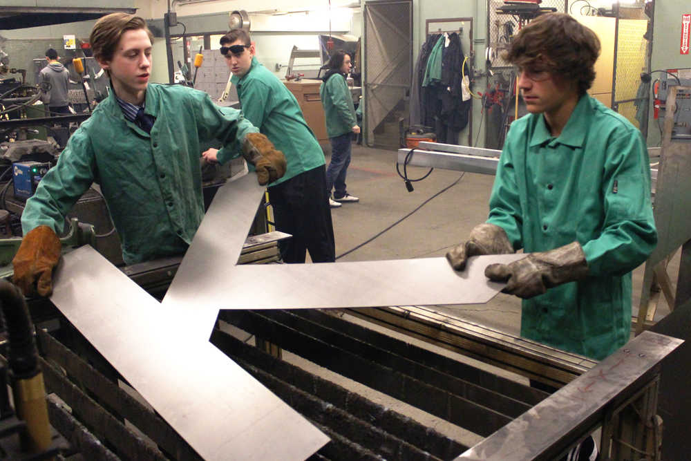 Ben Boettger/Peninsula Clarion Kenai Central High School freshmen Jude Gabriel (left) and Damien Redder lift the fresh-cut "K" - part of the Kenai sign the two are making - from a plasma cutter table  on Wednesday, Feb. 3 at Kenai Central High School.