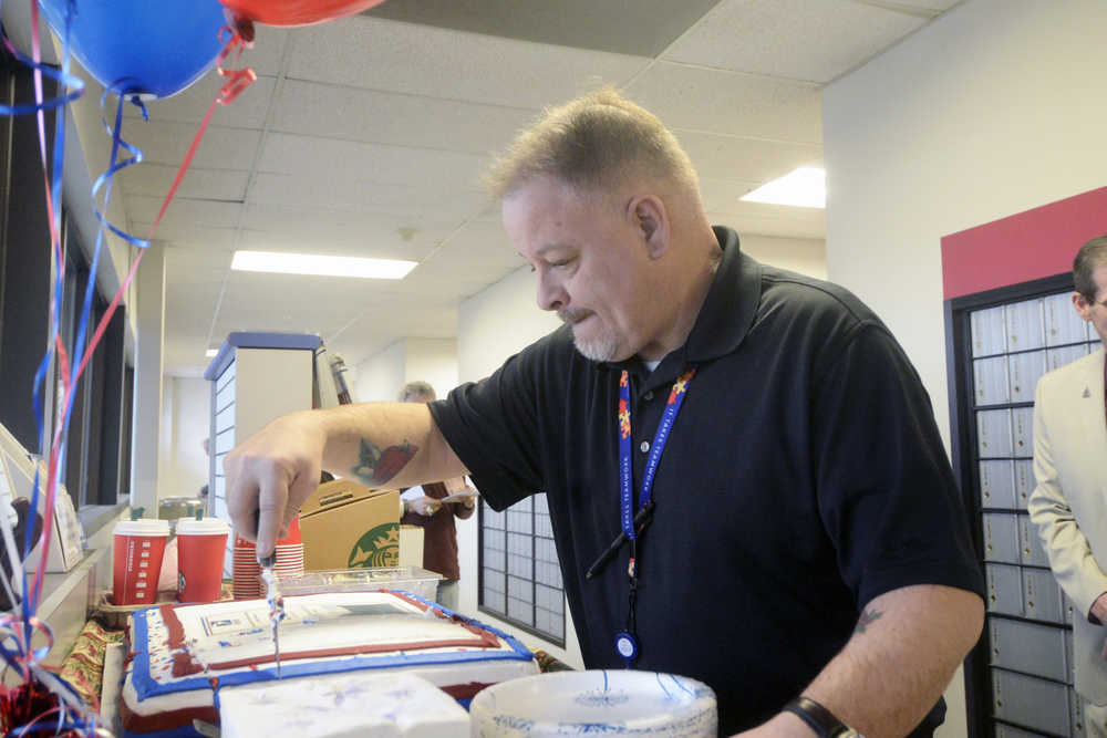 Photo by Megan Pacer/Peninsula Clarion John Tuttle cuts a celebratory cake after being sworn in as Soldotna's new postmaster on Thursday, Feb. 4, 2016 at the Soldotna Post Office in Soldotna, Alaska.