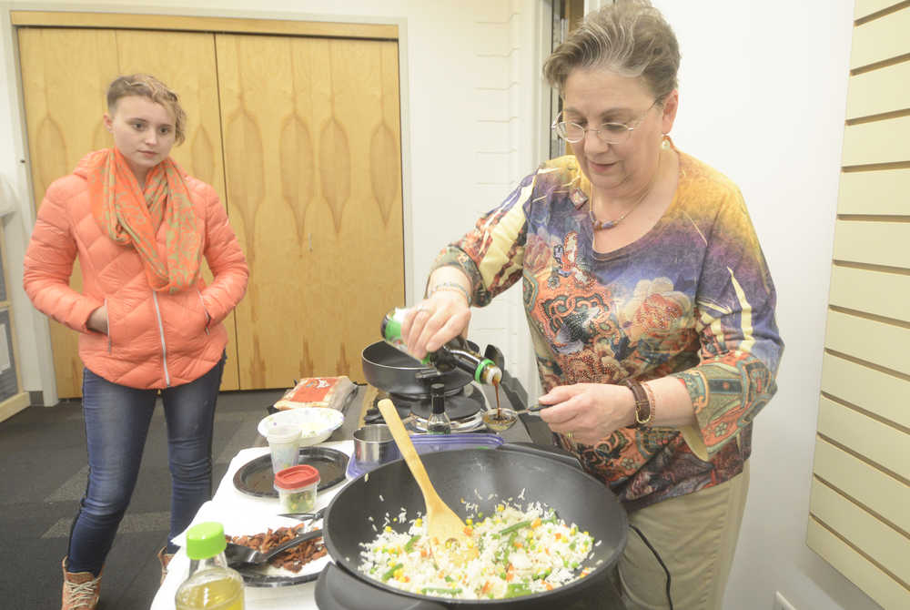 Photo by Megan Pacer/Peninsula Clarion Library Aide Amy Murrell-Haunold pours oil into a dish of fried rice while Kenai resident Ivy Howland looks on during a cooking demonstration on Monday, Feb. 8, 2016 at the Kenai Community Library in Kenai, Alaska.