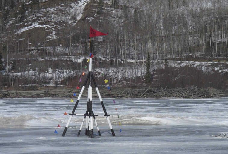 FILE - In this April 12, 2012 file photo, a red flag is whipped by wind on a tripod sitting on the frozen Nenana River on, in Nenana, Alaska. The tripod serves as the basis for Alaska's biggest guessing game, with people buying tickets to guess when the ice will give out and the tripod will fall into the river. Some states have a lottery. In Interior Alaska, it's the Ice Classic, the annual guessing game of when the Tanana River ice goes out. The spring tradition is celebrating its 100-year anniversary this year. (AP Photo/Mark Thiessen, File)